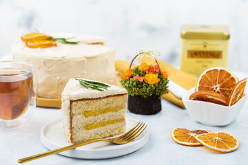 Obraz na płótnie Canvas Piece of Multi layer orange cake topped with slice of orange, sliced ​​orange and rosemary leaves.Placed in a plate and with a spoon placed on its side.Coffee time. Eat with coffee