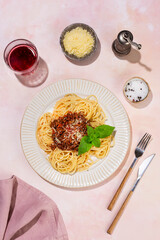 Bolognese spaghetti in a white plate on a light pink background. View from above.
