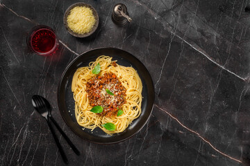 Delicious mouth-watering classic Italian spaghetti pasta with tomato sauce, parmesan cheese and basil on a plate on a dark table. Top view, horizontal