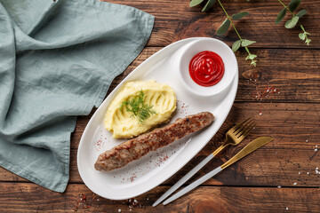 Grilled sausage with herb potatoes and ketchup, tasty summer picnic dish, on a dark wooden background