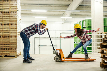 Two playful workers having fun with forklift in a warehouse.