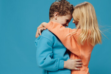 cute, joyful, loving children of school age stand on a blue background and gently hug each other.