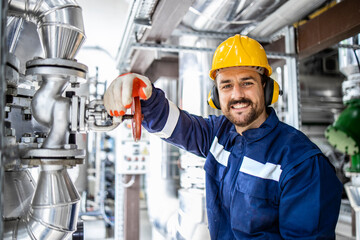 Portrait of smiling bearded refinery engineer or worker standing by pipes in oil production...