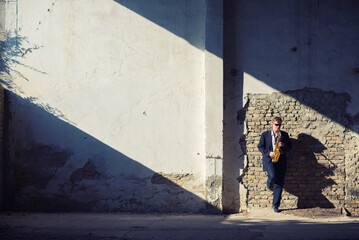 Man playing jazz on saxophone in the abandoned factory building on a sunny summer day
