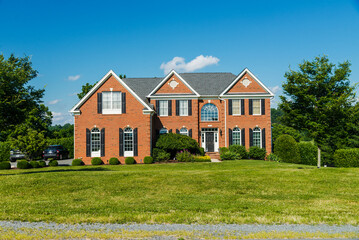 Front view of a large brick country house. Large freshly cut lawn and trees in the foreground.