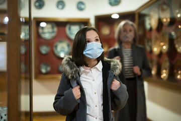 Obraz na płótnie Canvas Cute interested preteen girl wearing protective face mask exploring artworks in modern museum of applied arts. Forced precautions in pandemic