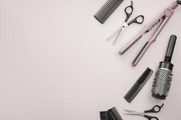 Scissors, combs, brushes and a hair straightener on a pale pink background.