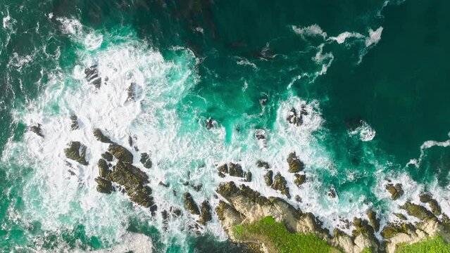 Aerial top view 4k footage by drone of ocean blue waves break on high cliff of a rocky mountain. Danger sea waves on a beach, 17-mile drive scenic route on West Coast California USA, tourism concept