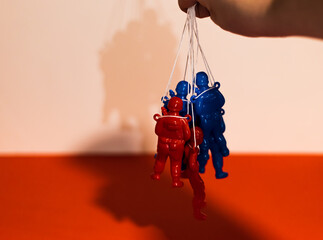 Red and blue Russian soldiers held like puppets by a dictator’s hand on red and white background....