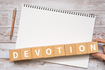 忠誠・献身のイメージ｜「DEVOTION」と書かれたブロック、ノート、ペン、手
