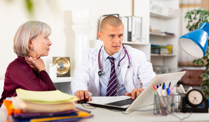 Fototapeta premium Senior woman complaining about sore throat to male doctor during medical consultation.
