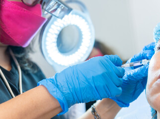 Close-up of a female doctor applying hyaluronic acid with a syringe to a patient illuminated by a...