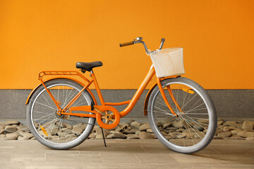 Modern color bicycle with basket near orange wall outside