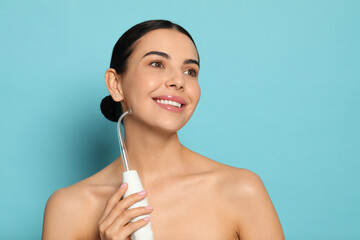 Woman using high frequency darsonval device on light blue background. Space for text