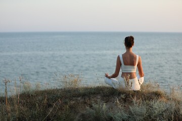 Naklejka na ściany i meble Woman meditating near sea, back view. Space for text