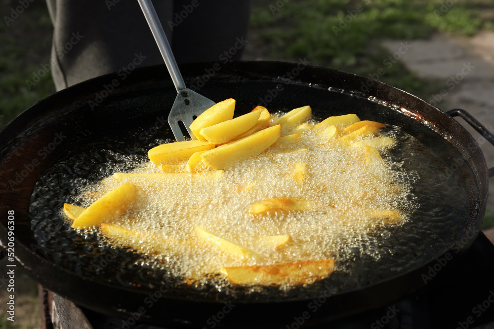 Wall mural Cooking delicious potato wedges on frying pan outdoors