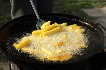 Cooking delicious potato wedges on frying pan outdoors