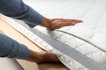 Man touching soft white mattress indoors, closeup