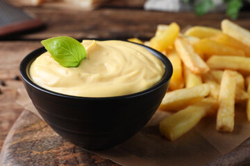 Delicious French fries and cheese sauce with basil on wooden table, closeup