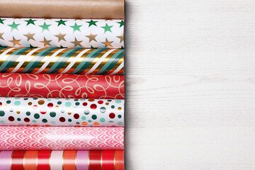 Different colorful wrapping paper rolls on white wooden table, flat lay. Space for text