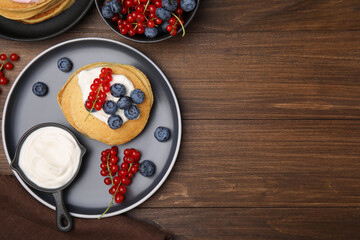 Tasty pancakes with natural yogurt, blueberries and red currants on wooden table, flat lay. Space for text