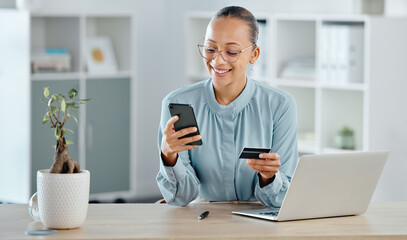 Obraz na płótnie Canvas Female executive online shopping, buying with a corporate credit card on a phone. A smiling woman paying business bills, sitting at office desk with laptop. Happy lady making a purchase on a website.