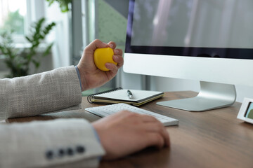 Man squeezing antistress ball while working with computer in office, closeup