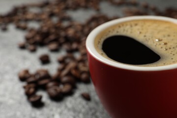 Cup of aromatic coffee and beans on grey table, closeup. Space for text
