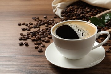 Cup of aromatic hot coffee and beans on wooden table, space for text