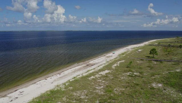 Aerial flight along a Gulf of Mexico beach that is secluded with someone enjoying some shade under umbrella