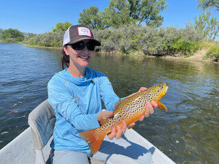 A beautiful woman posing with a brown trout that she caught fly fishing.