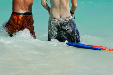 Rear view of two Mexican boys entering the sea with sand in their swimsuit bodies