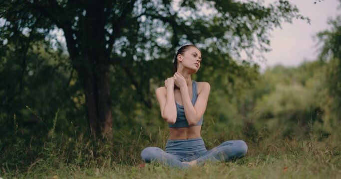 A woman after a sports workout kneads her neck muscles in the park, rest and health care