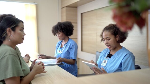 People making an appointment with medical staffs at reception desk in hospital. Medical staff and nurse - receptionist talking to patient in front of the reception counter in hospital.