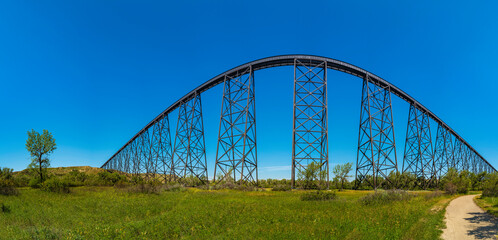 Abstract geometry and shapes of  Lethbridge Viaduct Railway Bridge over the meadow with a cottonwood tree in Lethbridge, Alberta, Canada. Arching effect of wide angle lens.