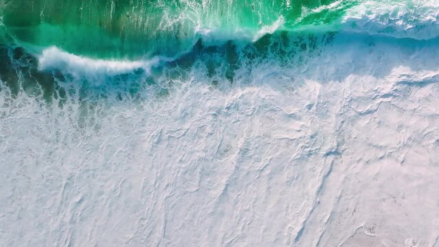 Waves of water of Pacific ocean or sea meet sandy beach during high tide and low tide. Whirlpools of the maelstrom of ocean waves on West Coast of California, USA. Aerial slow motion cinematic waves 