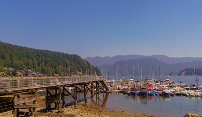 Obraz premium Boats moored near pier and beach at beautiful Deep Cove, BC, on a sunny day, with water-view homes in background.