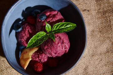 Flat lay. Delicious healthy raw vegan berry ice cream with ripe juicy fruits and lemon basil leaves in navy ceramic bowl