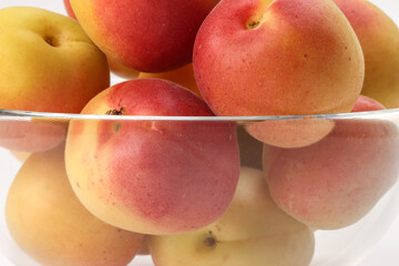 Fresh ripe juicy yellow orange red apricot fruit pile whole cut half slice seed in transparent glass bowl on white background