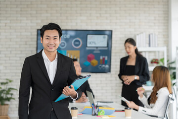 Portrait of Asian business man standing in meeting room with partner or colleagues blur background