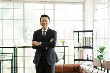 Asian, adult businessman and office. Portrait of Asian business man wear suit at the office. Smiling Asian business man standing with background modern office © amorn