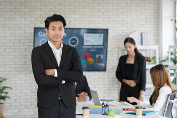 Portrait of Asian business man standing in meeting room with partner or colleagues blur background