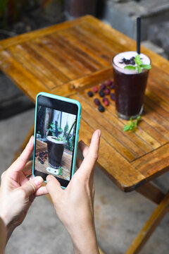 Hands holding a phone taking picture of mulberry tea for advertisement 