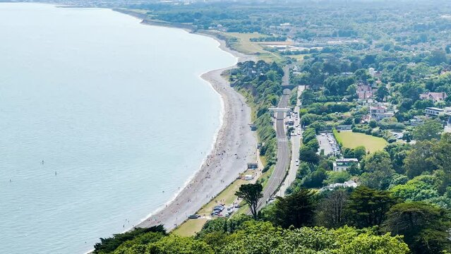 Killiney Beach with a lot of people on a sunny day, with a train station to the right and full car parks, Ireland.