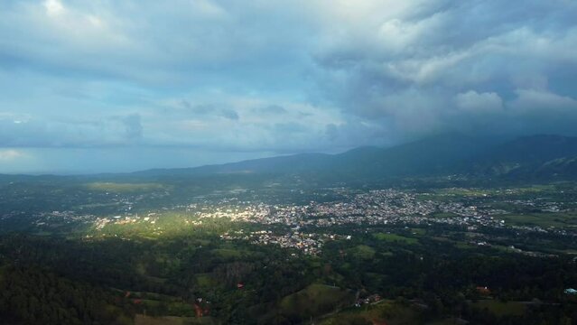 Aerial over mountain range covered with dense green forest and village in the valley. Jarabacoa, Dominican Republic. Beautiful scenery on a bright sunny day