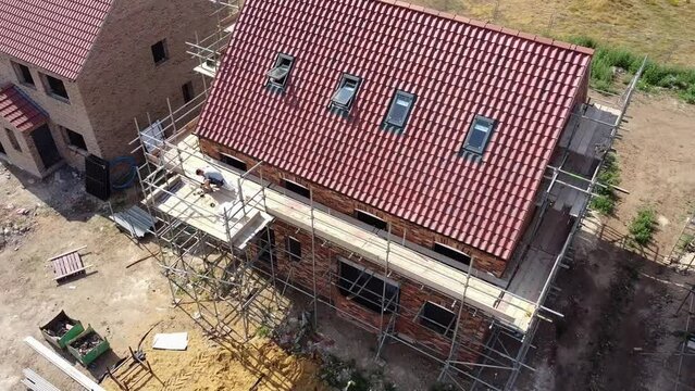 Rotating aerial view of a scaffolded new build house under construction, showing the front elevation and the gable end.