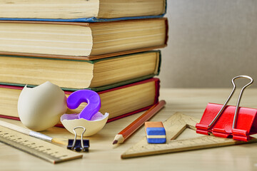 Fototapeta na wymiar a stack of books writing materials paper clips and a split chicken egg with a question mark inside on the table the concept of knowledge education school