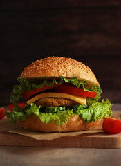 fresh hamburger with cutlet, cucumber, tomato and salad on a wooden board and dark background