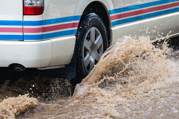 White van passing through flooded road. Driving car on flooded road during flood caused by torrential rains. Flooded city road with large puddle. Splash by car through flood water. Selective focus. © JinnaritT