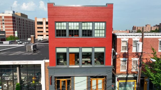 Rising aerial shot of modern, industrial style building in small city setting. Telephone wires and brick city buildings featured.